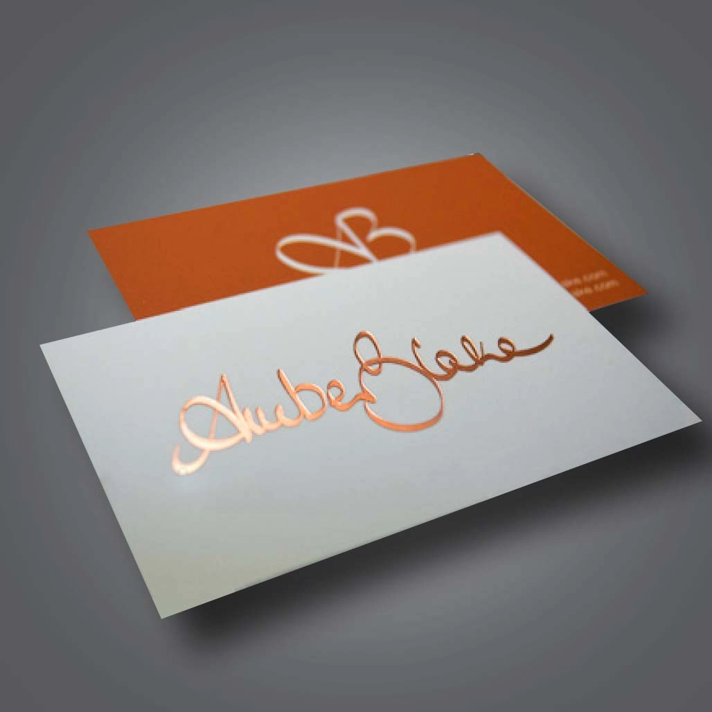 A white business card with gold metallic foil text stacked on top of an orange business card with white metallic foil text